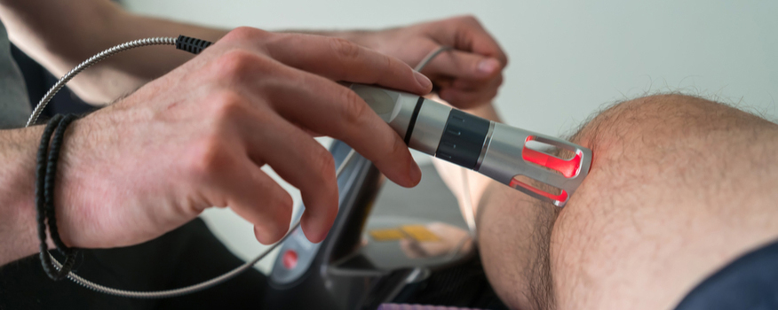 Hand using Class IV cold laser therapy device on a patient's knee, illustrating non-invasive pain relief and healing.